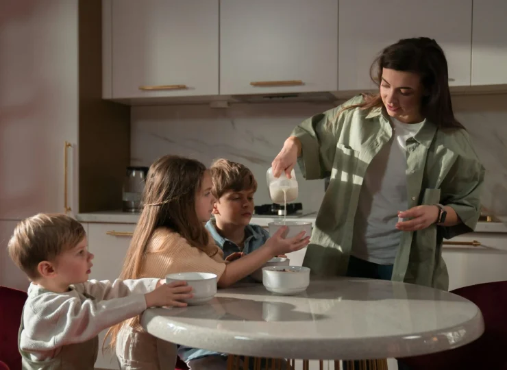 madre sirviendole leche de desayunar a sus 3 hijos